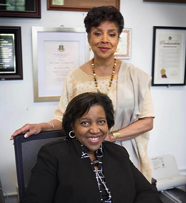 Phylicia Rashad stands behind a seated Dr. Evelyn Collins in an office hung with framed awards and proclamations.