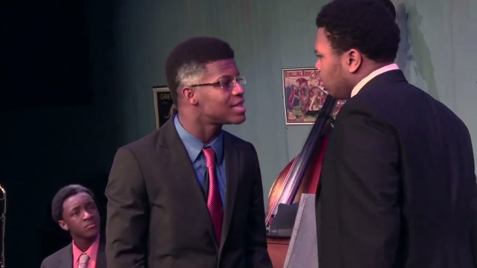 Actors in suits face each other on stage in a scene from Ma Rainey's Black Bottom, a double bass behind them.
