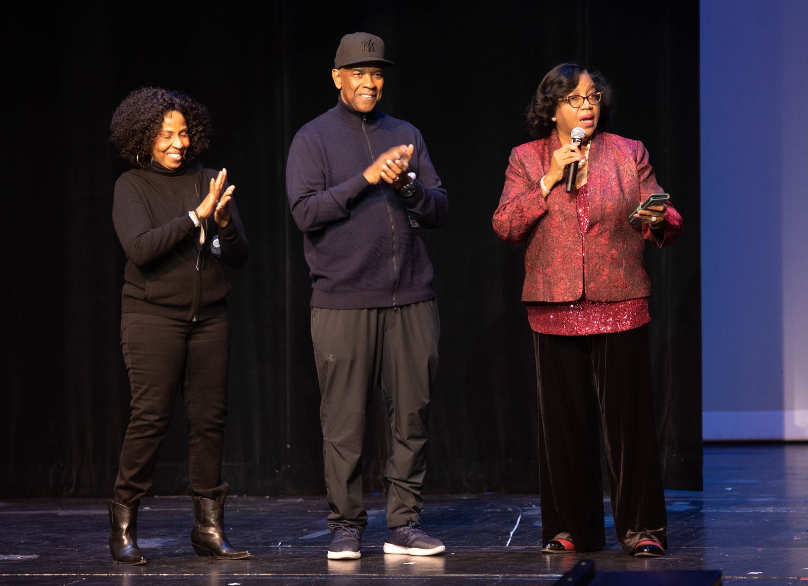 Denzel Washington and Pauletta Washington applaud on stage as Dr. Evelyn Collins speaks into a microphone.