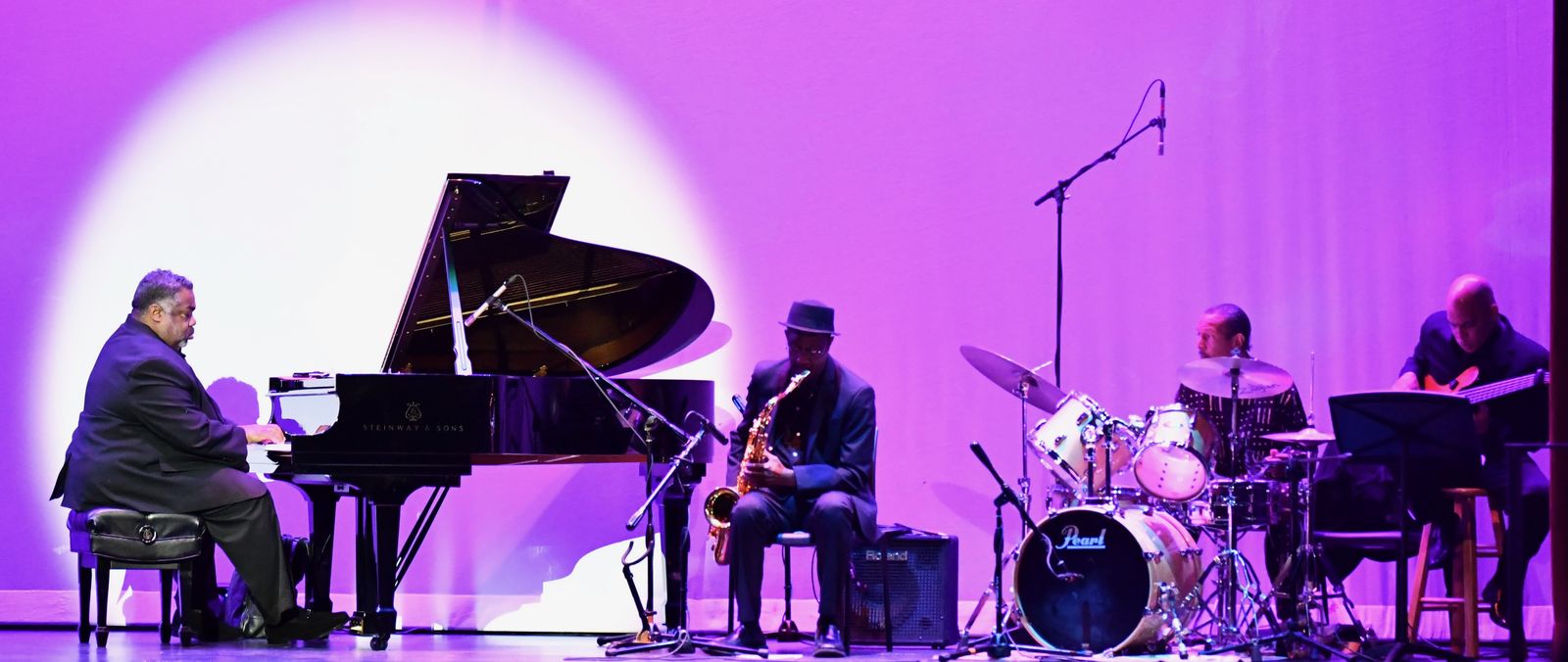 Musicians performing on stage with grand piano, saxophone, drums, and guitar